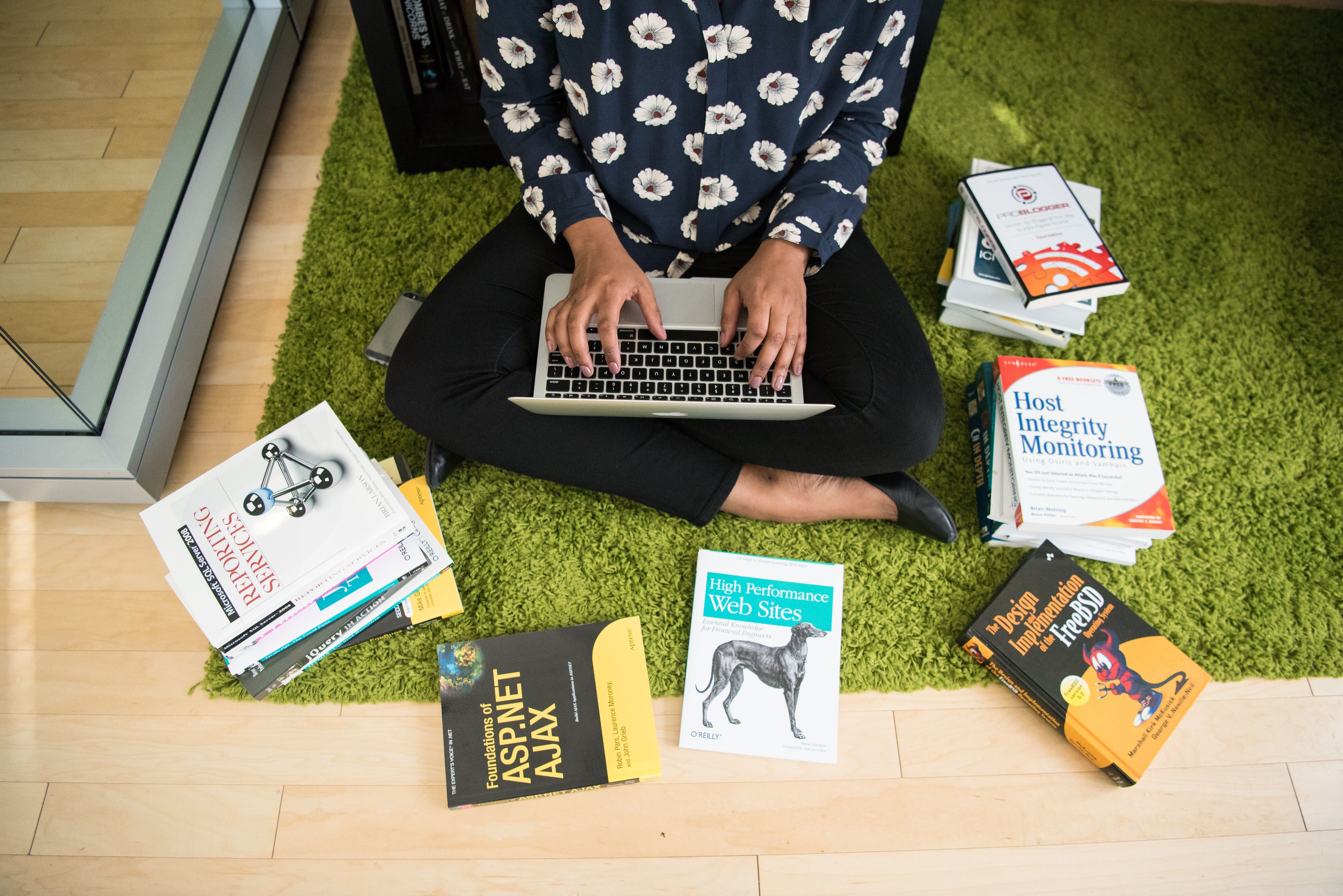 Technology book layed out around a person sitting on the floor with a laptop